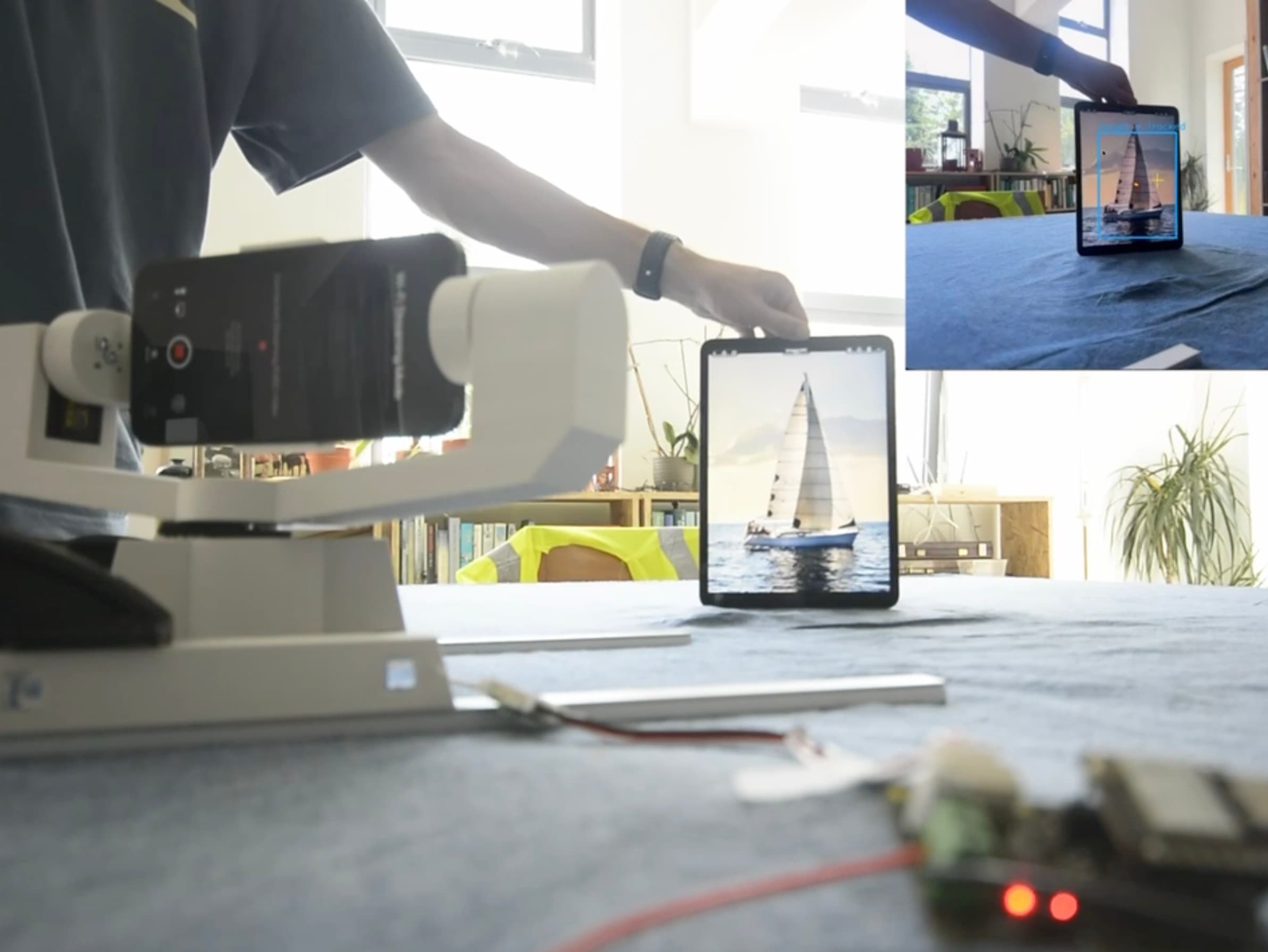 The gimbal pointing its phone at a sailboat on an iPad as the iPad is moved across the table, with the camera's tracked view inset